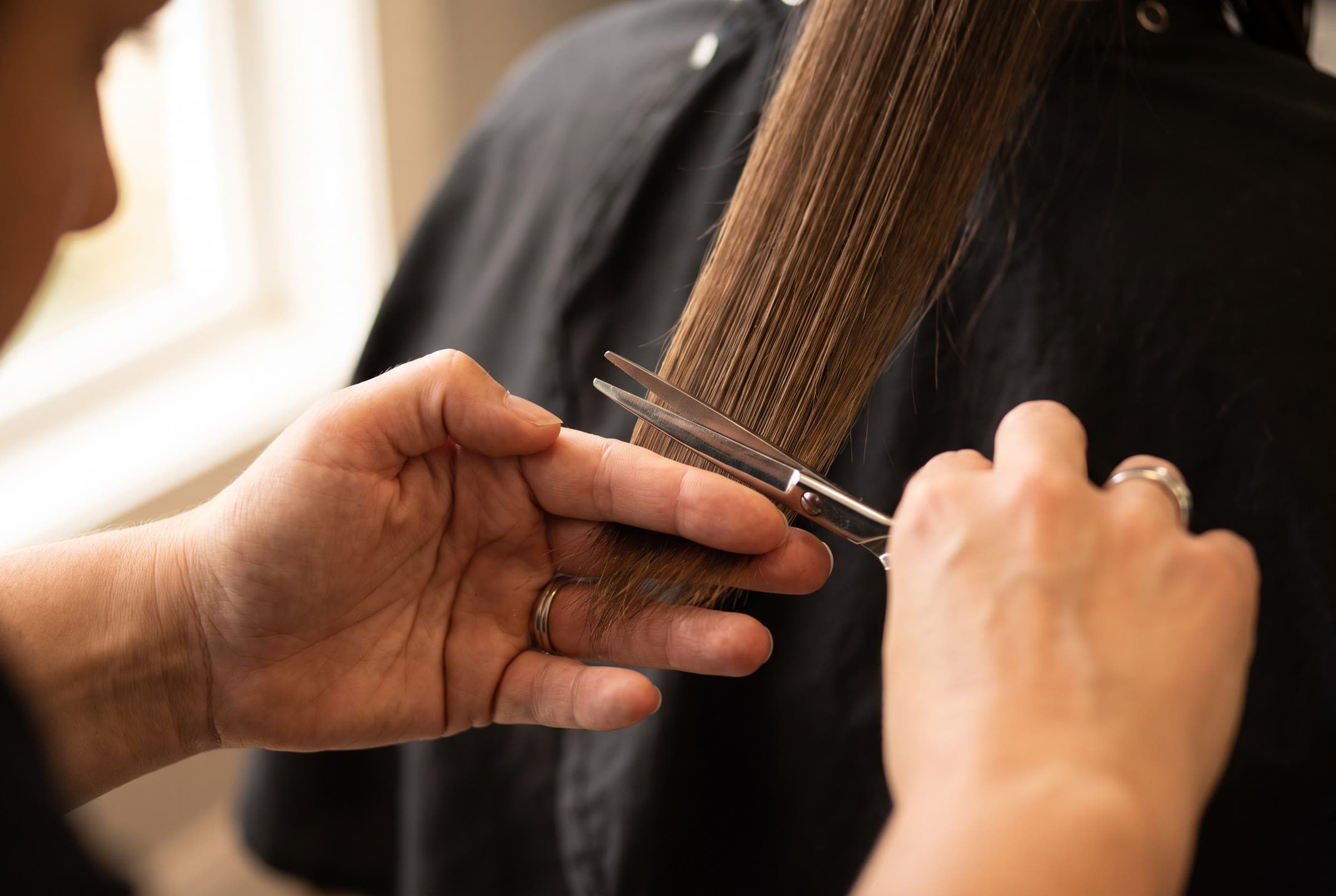 Nahaufnahme: Die Hände einer Friseurin halten eine Haarsträhne und setzen mit der Schere einen präzisen Schnitt.